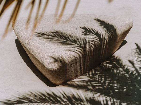 Schatten von Palmblättern die sich am Boden und auf einem Sitzstein abbilden